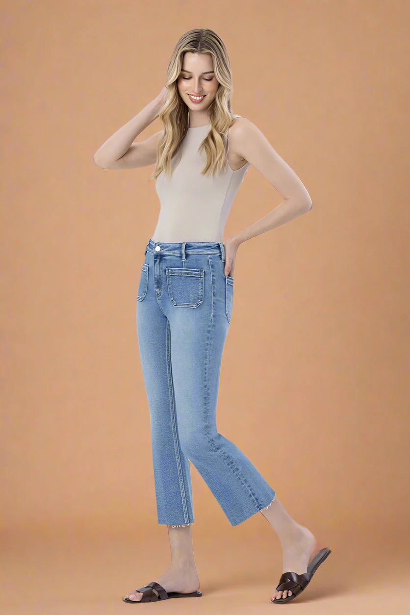 Woman wearing light blue jeans and a beige top on a plain background.