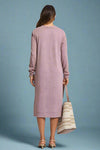 Woman wearing a long pink dress holding a striped bag on a plain background