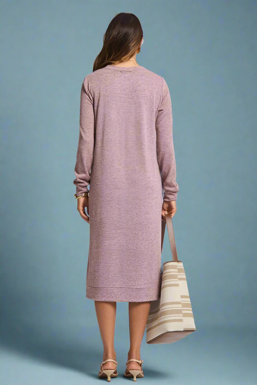 Woman wearing a long pink dress holding a striped bag on a plain background
