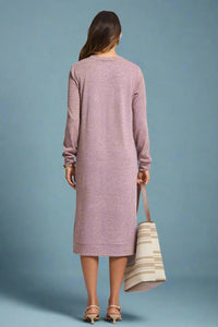 Woman wearing a long pink dress holding a striped bag on a plain background