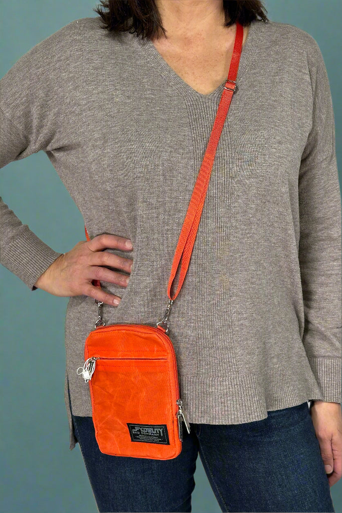 Model is wearing an orange colored small crossbody bag with zipper pouches and removable straps. 