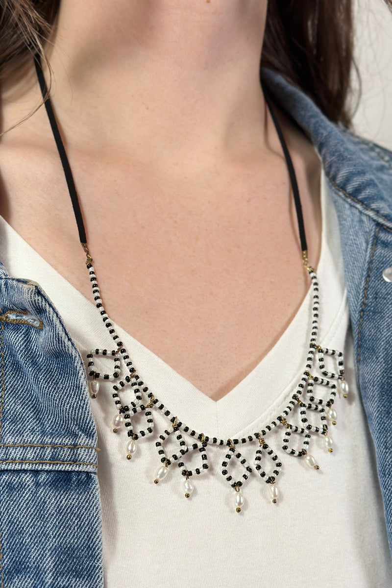 Model is wearing a black and white beaded necklace. 