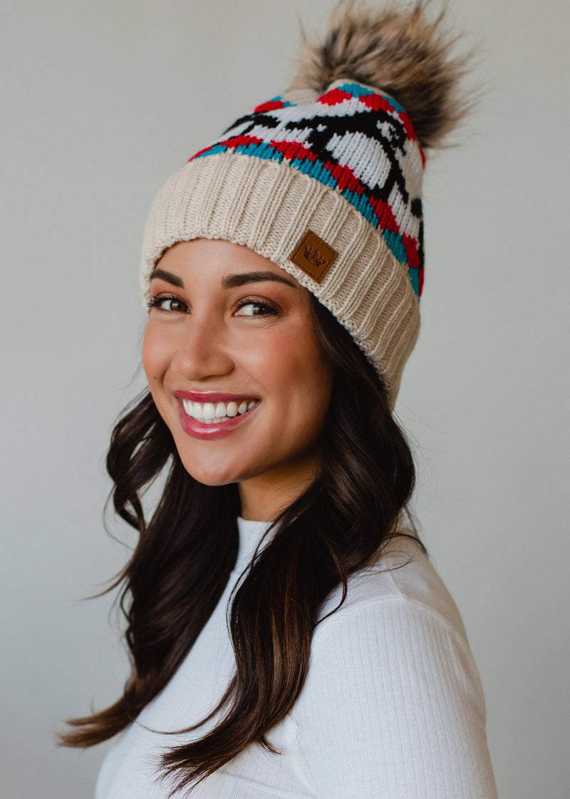 Woman wearing a colorful beanie with a pom-pom against a neutral background