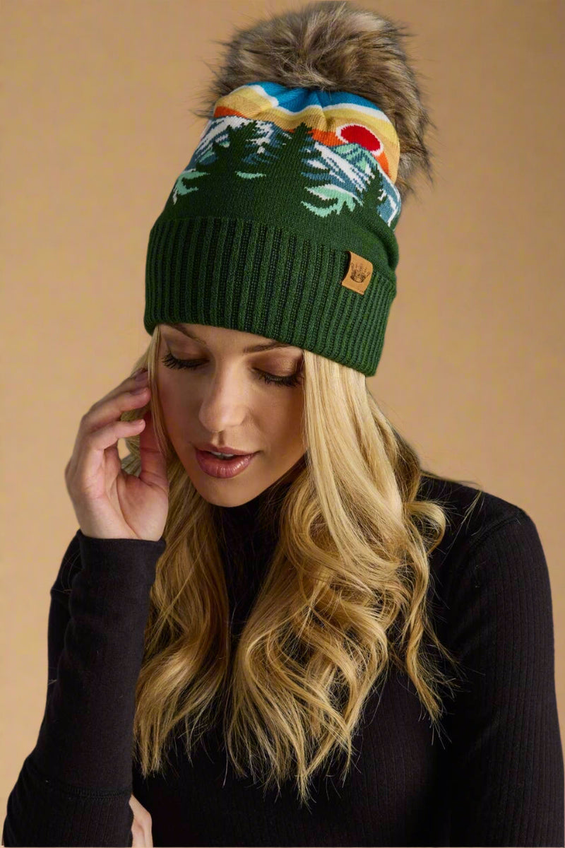 Woman wearing a green beanie with colorful design and fur pom-pom on a gray background