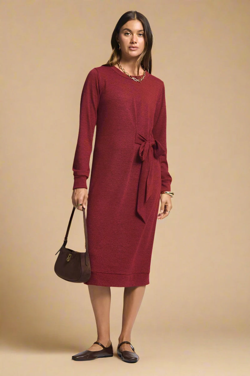 Woman wearing a red dress with a belt, holding a brown handbag on a plain background