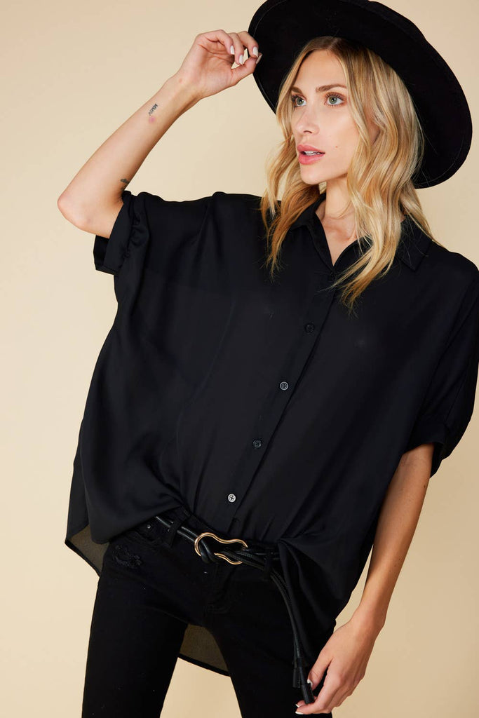 Model is wearing and oversized button down shirt in black featuring short dolman sleeves. 