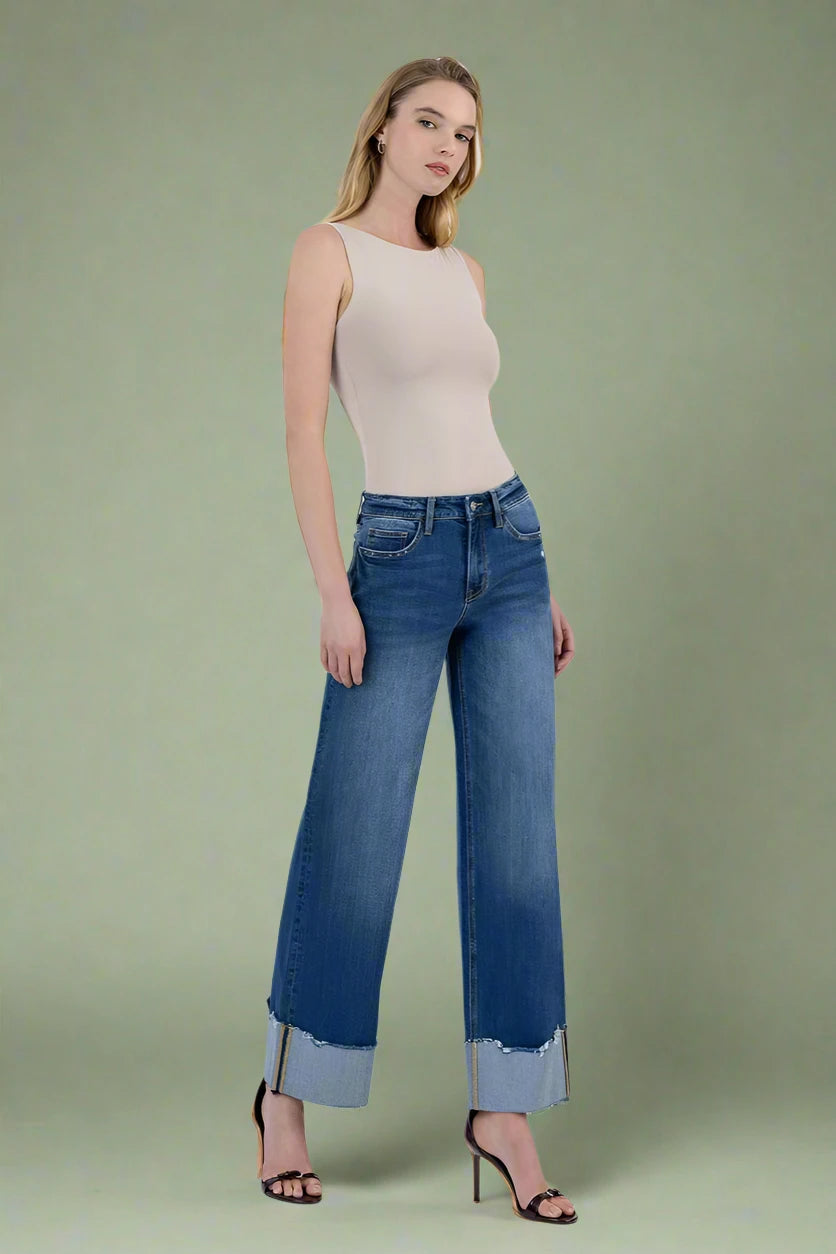 Woman wearing a beige sleeveless top and blue jeans on a plain background.