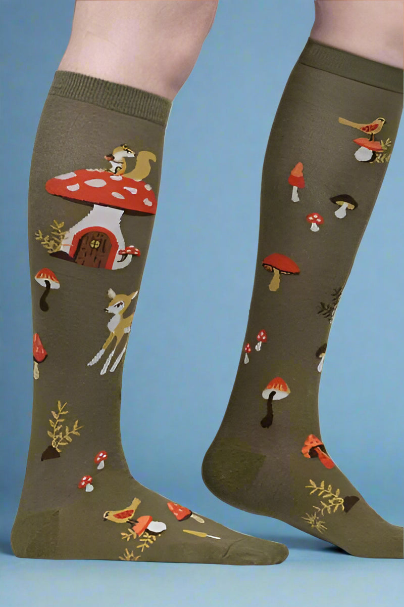 Green knee-high socks with mushroom and animal pattern worn by a person on a white background