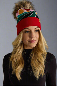 Woman wearing a colorful knit beanie with a pom-pom on a gray background