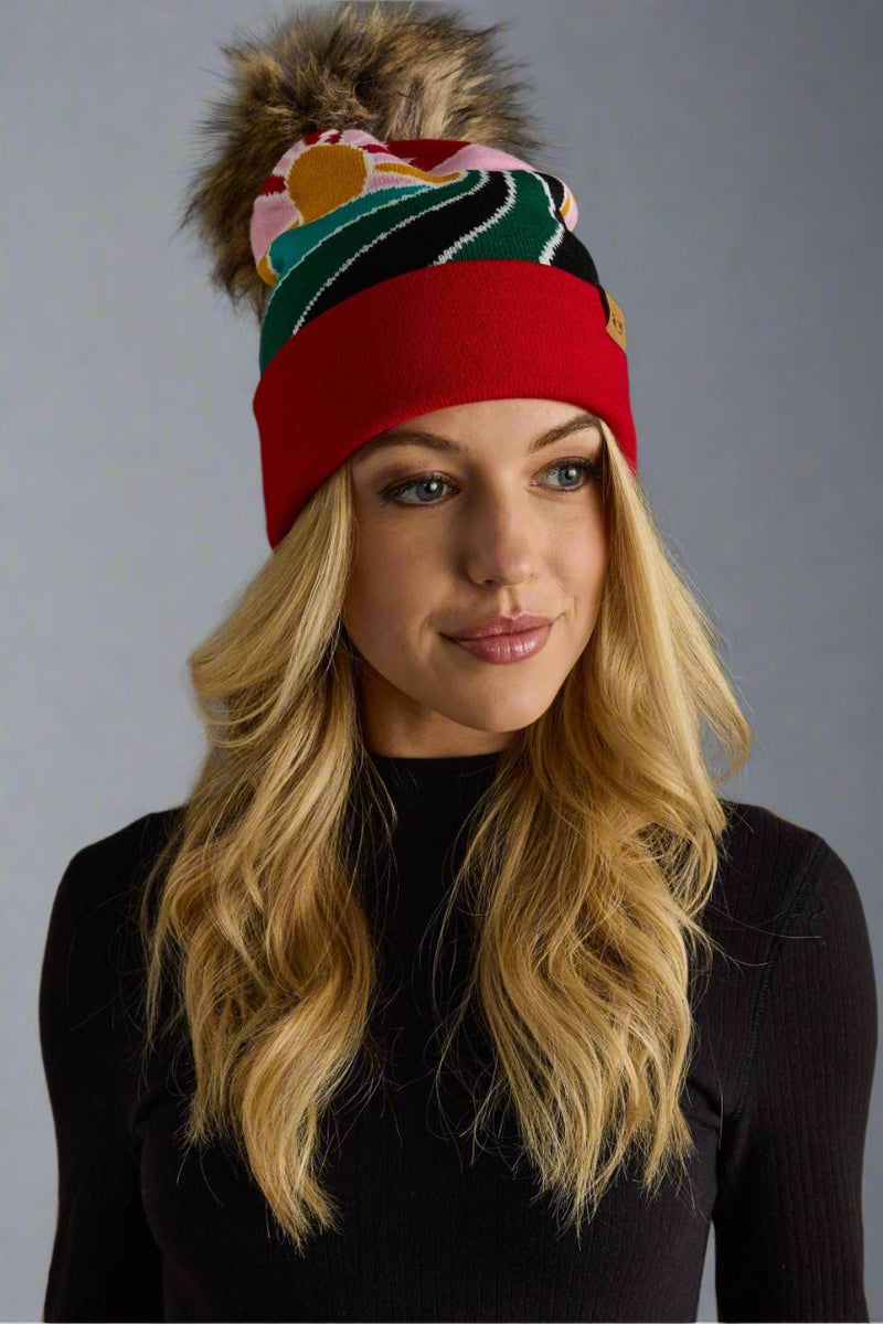Woman wearing a colorful knit beanie with a pom-pom on a gray background