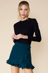 Model is wearing a teal skort with wrap detail and ruffled hem. 
