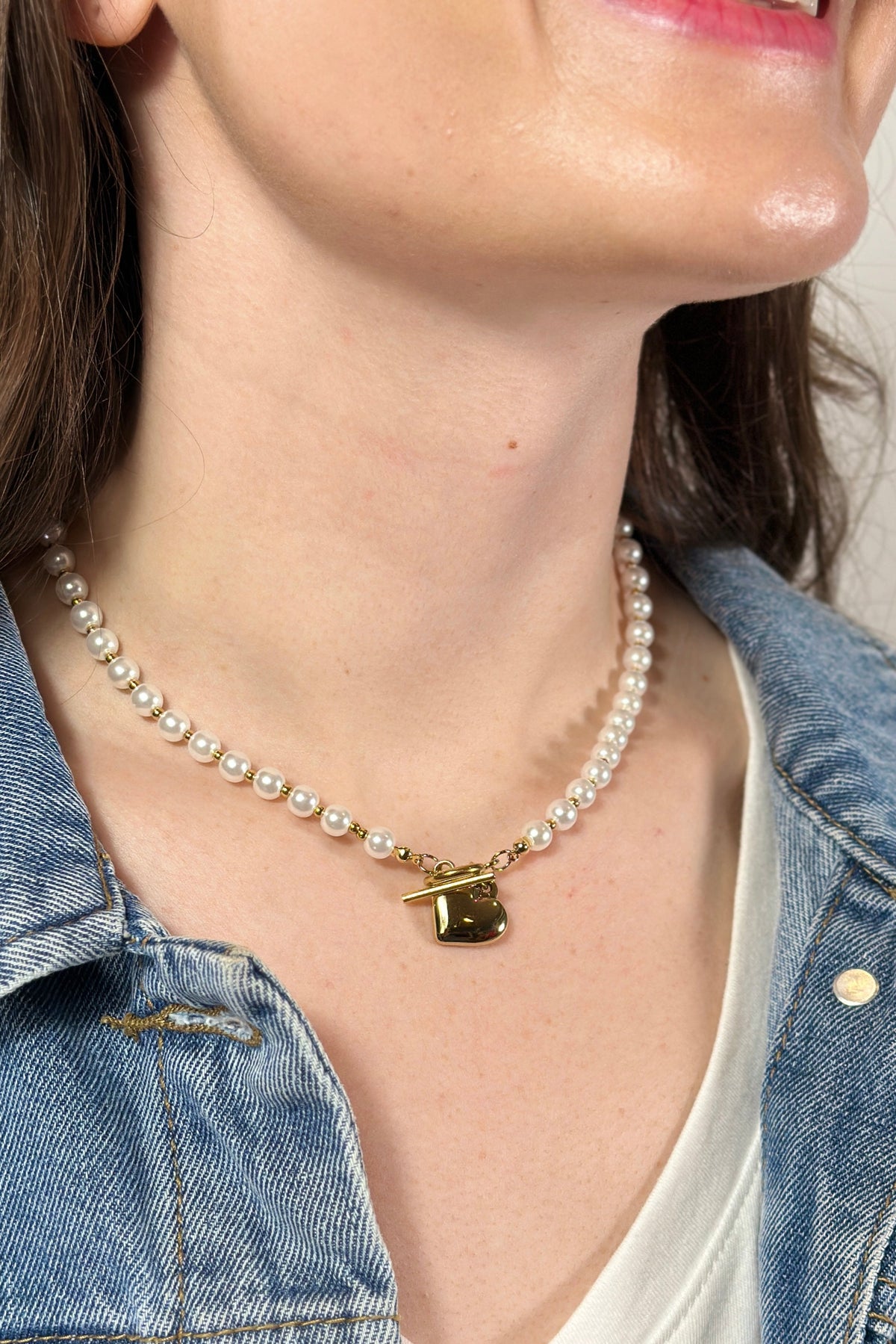 Model is wear a short pearl necklace with gold heart charm. 