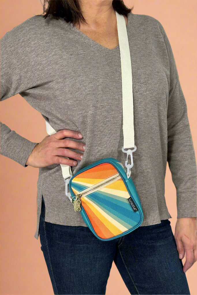 Model is wearing a small retro rainbow crossbody bag with an external zipper pocket and adjustable canvas strap. 