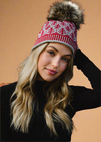 Woman wearing a red and white patterned beanie with a fur pom-pom against a dark background