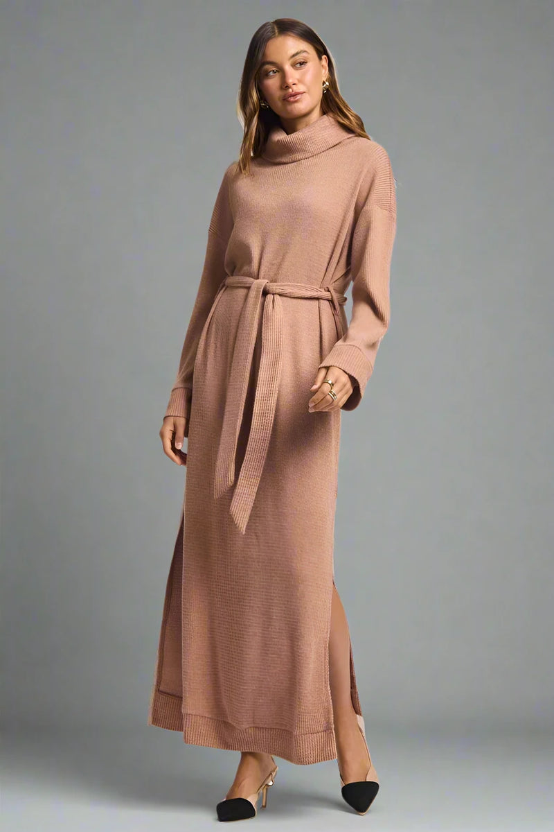 Woman wearing a long brown dress with a belt on a plain background.