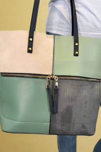 Model is carrying a large color block tote bag with external zippers in olive sage green. 