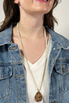 Model is wearing a long beaded necklace with gold teardrop pendant. 