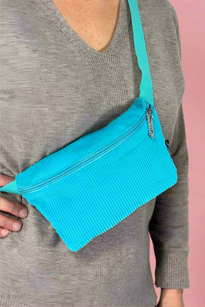 Model is wearing a neon blue corduroy fanny pack bag with an adjustable canvas strap. 