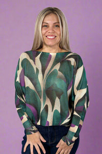 Model is wearing a light knit sweater with dolman sleeves and a vibrant dark teal and purple pattern. 