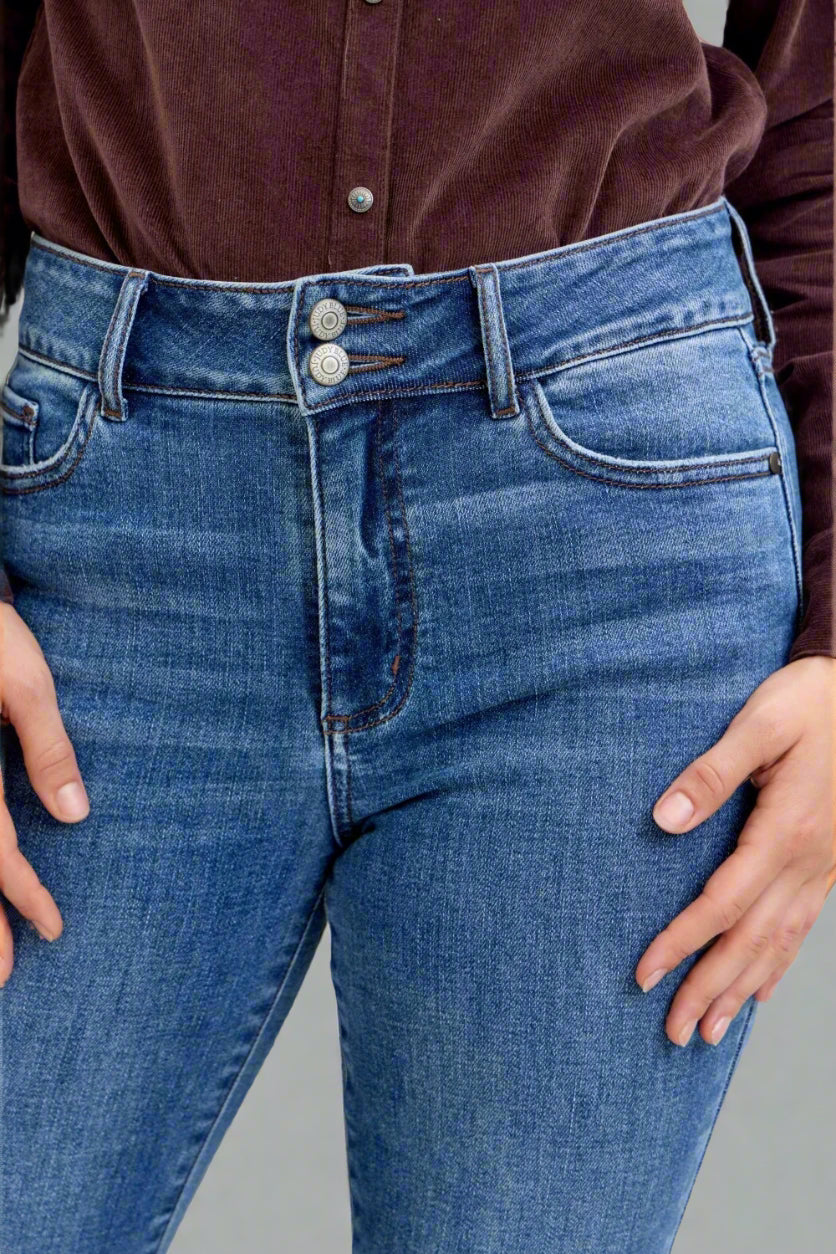 Close-up of blue jeans with a button and zipper, worn by a person.