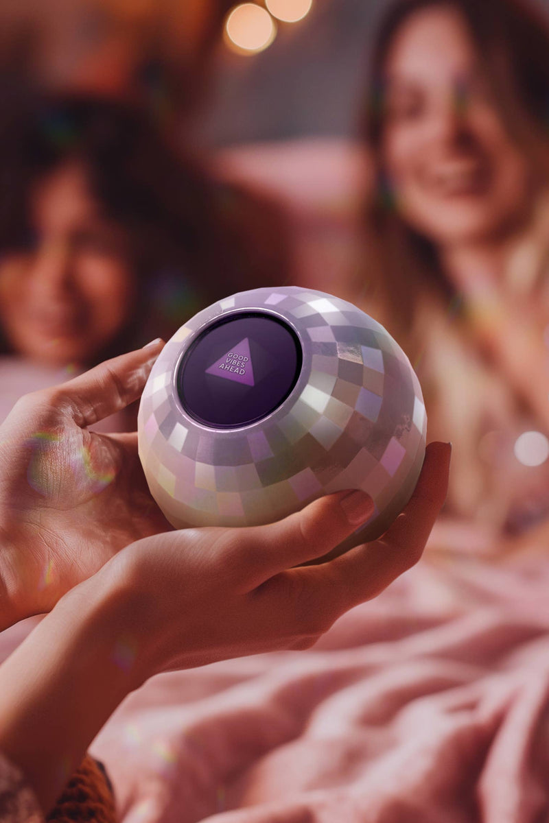 Person holding a colorful, disco ball-like device with people in the background.