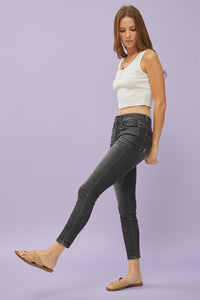 Woman wearing a white sleeveless top and black jeans on a plain background