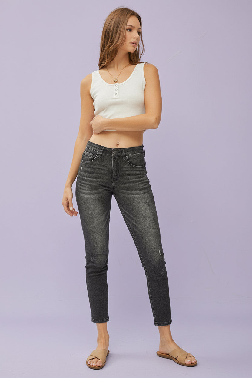 Woman wearing a white tank top and black jeans on a plain background