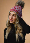 Woman wearing a red and white patterned knit hat with a fur pom-pom against a black background