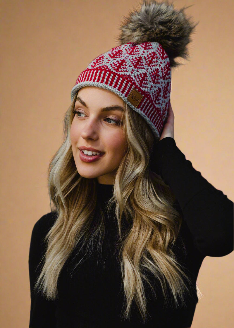 Woman wearing a red and white patterned knit hat with a fur pom-pom against a black background