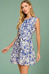 Woman wearing a blue and white floral dress on a plain background.