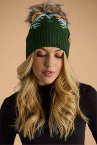 Woman wearing a green knit beanie with colorful pom-pom against a gray background
