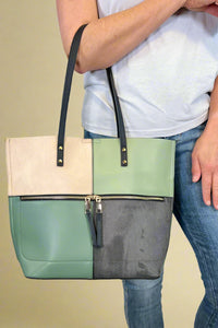 Model is carrying a large color block tote bag with external zippers in olive sage green. 