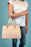 Model is wearing a large natural colored satchel with multiple compartments. 