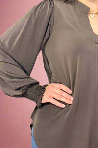 Person wearing a brown long-sleeve top with a plain background.