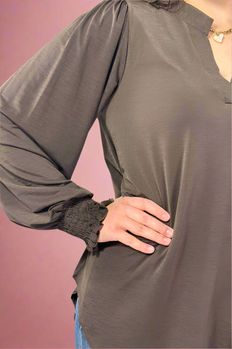 Person wearing a brown long-sleeve top with a plain background.