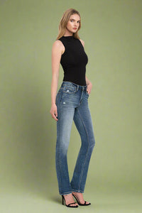 Woman wearing blue jeans and a black top on a plain background.