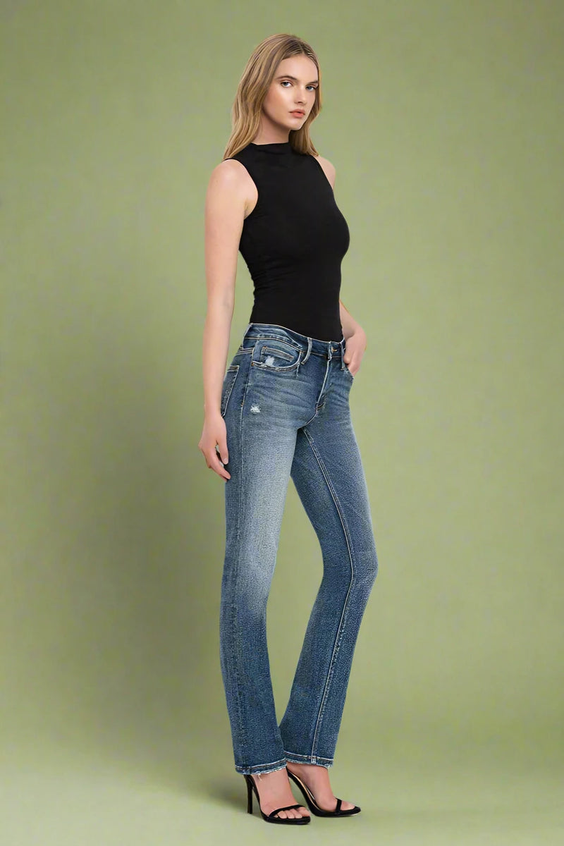 Woman wearing blue jeans and a black top on a plain background.