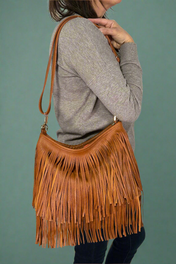 Model is wearing a tan colored crossbody purse that features layers of fringe.