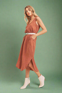 Woman wearing a rust-colored dress with white boots on a beige background