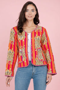 Woman wearing a colorful tiger patterned quilted jacket with a pink background.