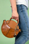 Model is carrying a small circle purse with braided handle, gold keychain and exterior pockets. Includes a cross body strap. 