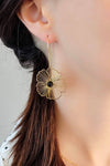 Model wears a dangling, hoop earring with a delicate, gold stainless steel flower decorated with a semi-precious, agate stone.
