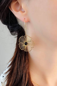 Model wears a dangling, hoop earring with a delicate, gold stainless steel flower decorated with a semi-precious, agate stone.
