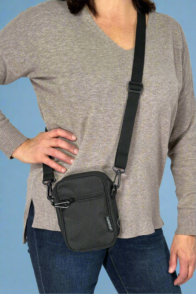 Model is wearing a small black crossbody bag with an external zipper pocket and adjustable canvas strap. 