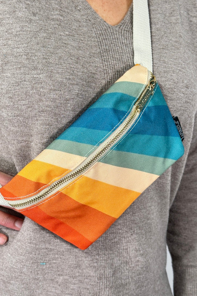 Model is wearing a retro rainbow printed fanny pack bag with an adjustable canvas strap. 