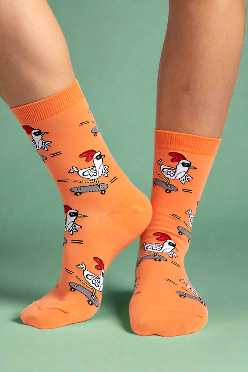 Orange socks with chicken designs worn by a person on a light gray background