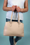 Model is wearing a large natural colored satchel with multiple compartments. 