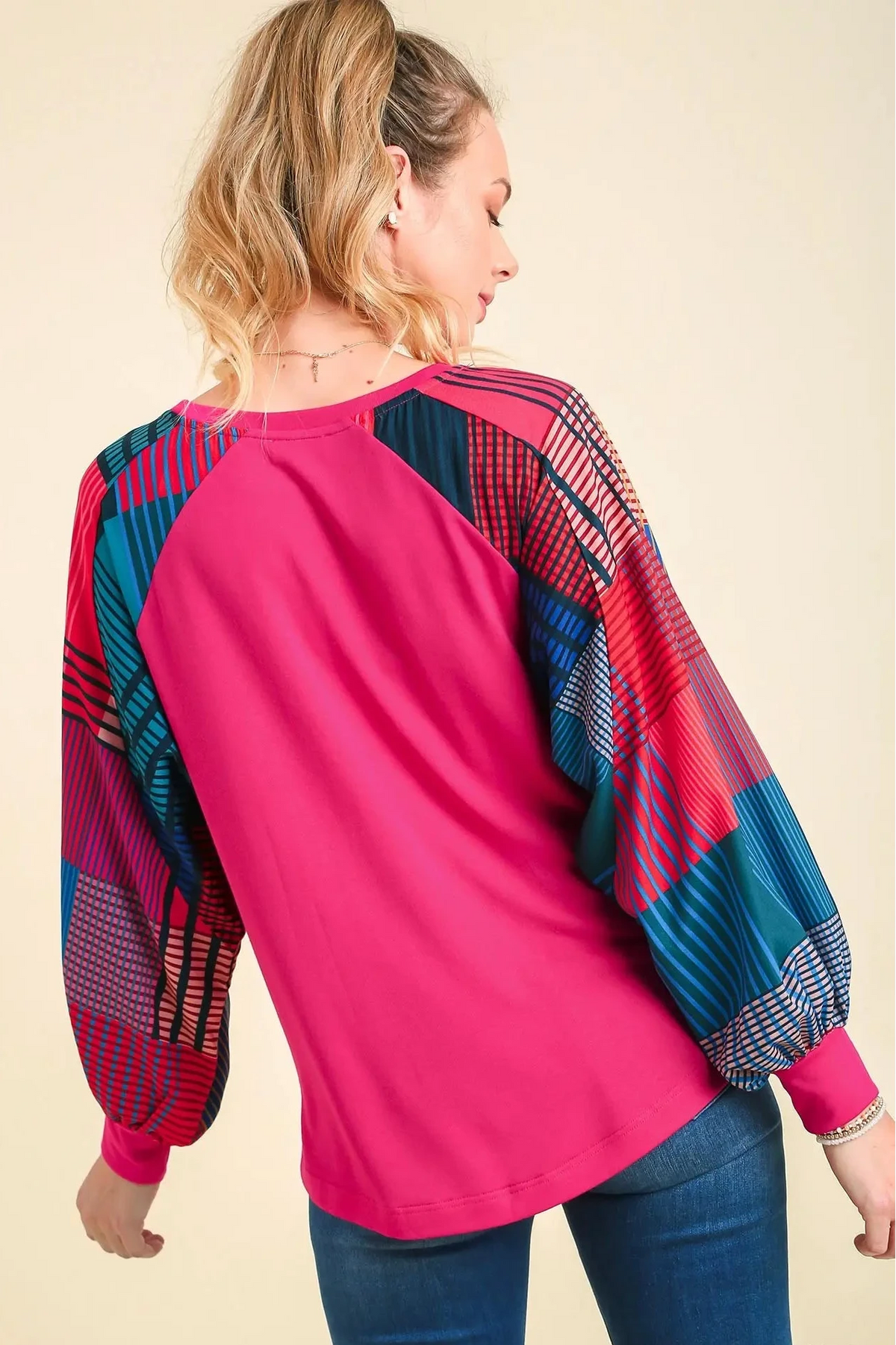 Woman wearing a pink long-sleeve top with colorful sleeves on a beige background