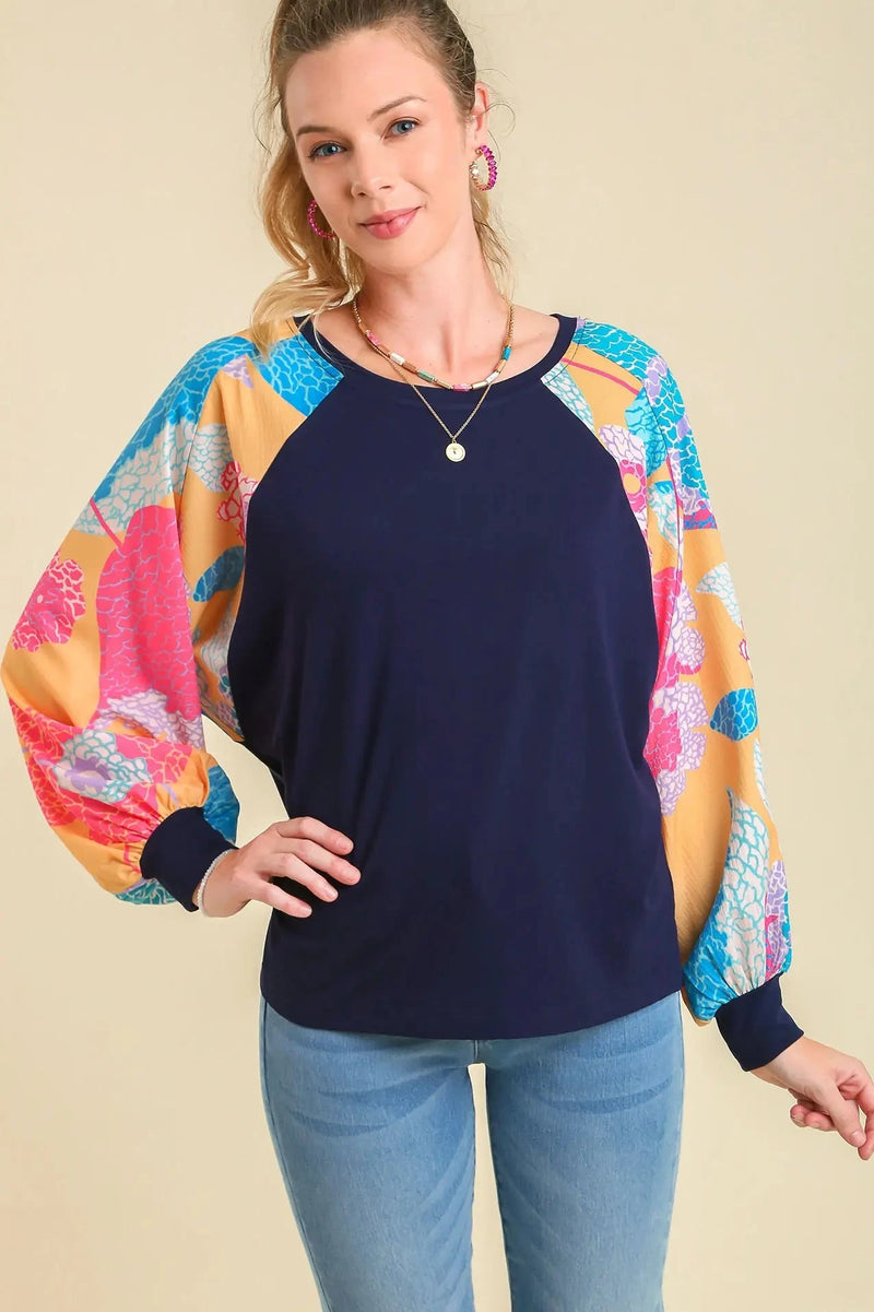 Woman wearing a navy blue top with colorful sleeves on a beige background
