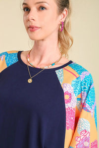 Woman wearing a navy blue top with colorful sleeves against a beige background